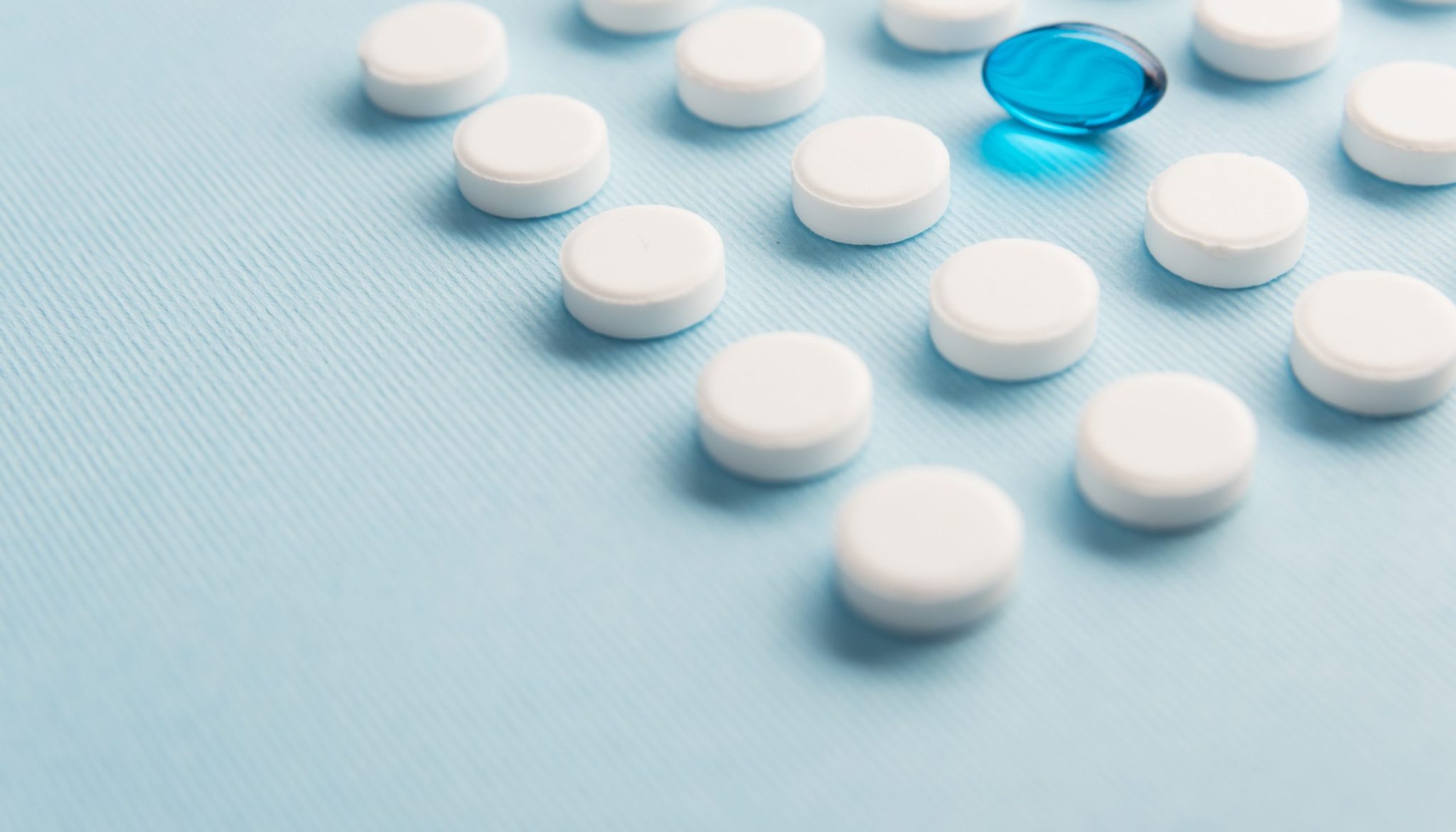Close up of one blue liquid capsule in a pattern of white tablets isolated