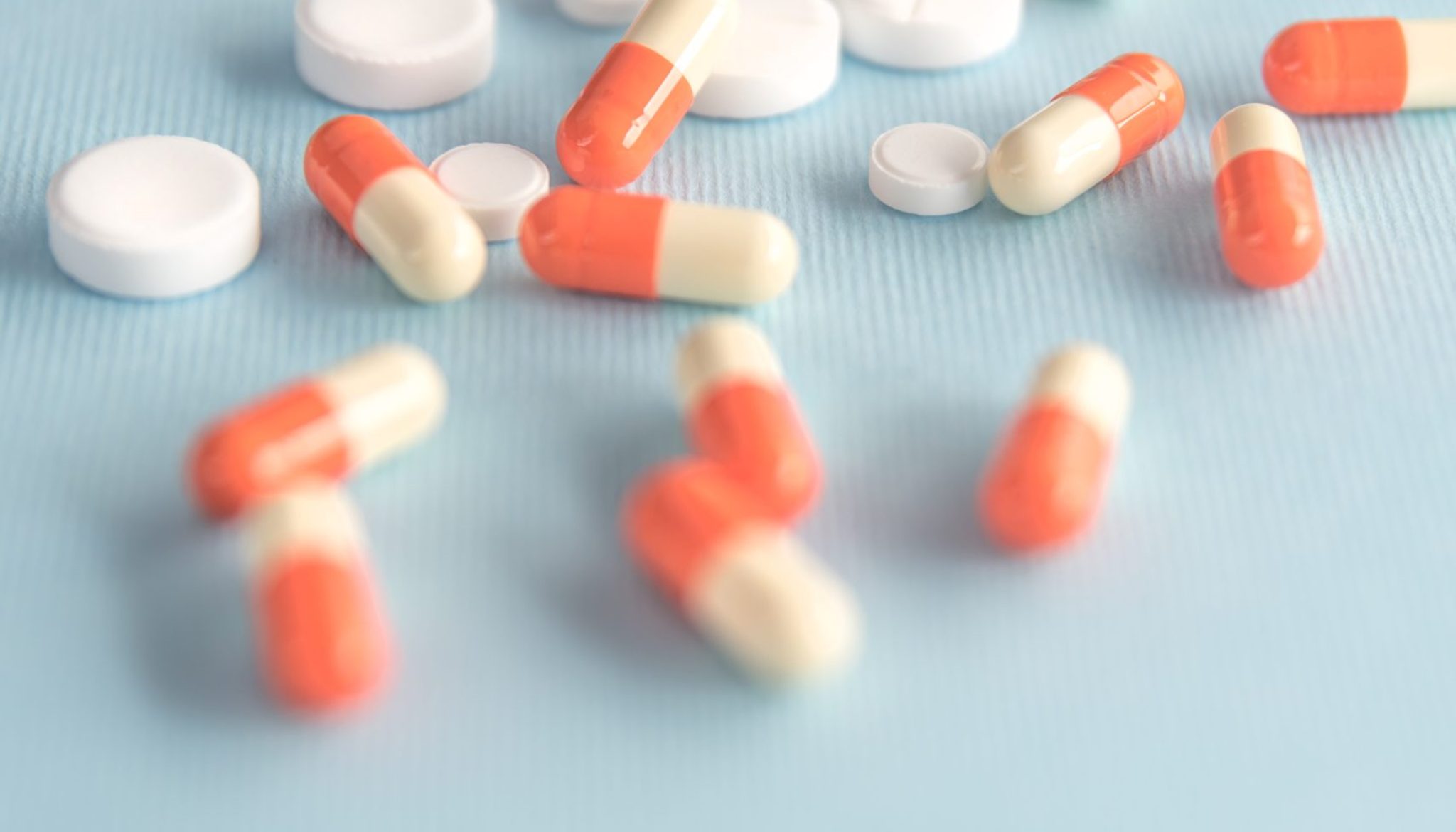Close up of two colored capsules and white pills spread all over isolated