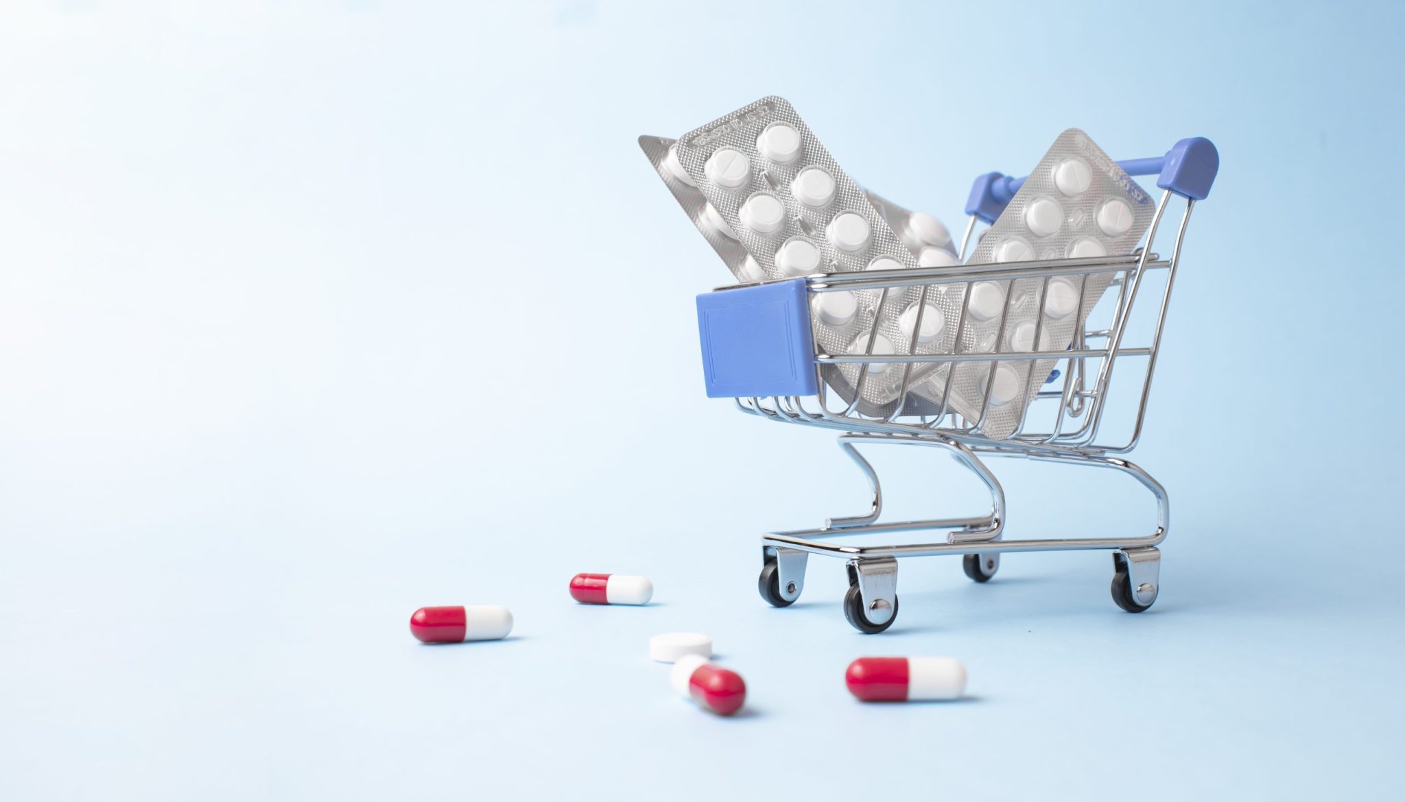 Shopping trolley cart made by pills on light blue background.